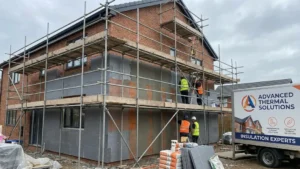 Ocieplenie domu 2026 - układanie styropianu na elewacji z rusztowaniem, pracownicy montują płytę izolacyjną