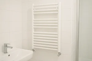 Biały grzejnik łazienkowy drabinkowy zamontowany na ścianie nowoczesnej łazienki z białymi płytkami ceramicznymi - wybór i montaż 2026